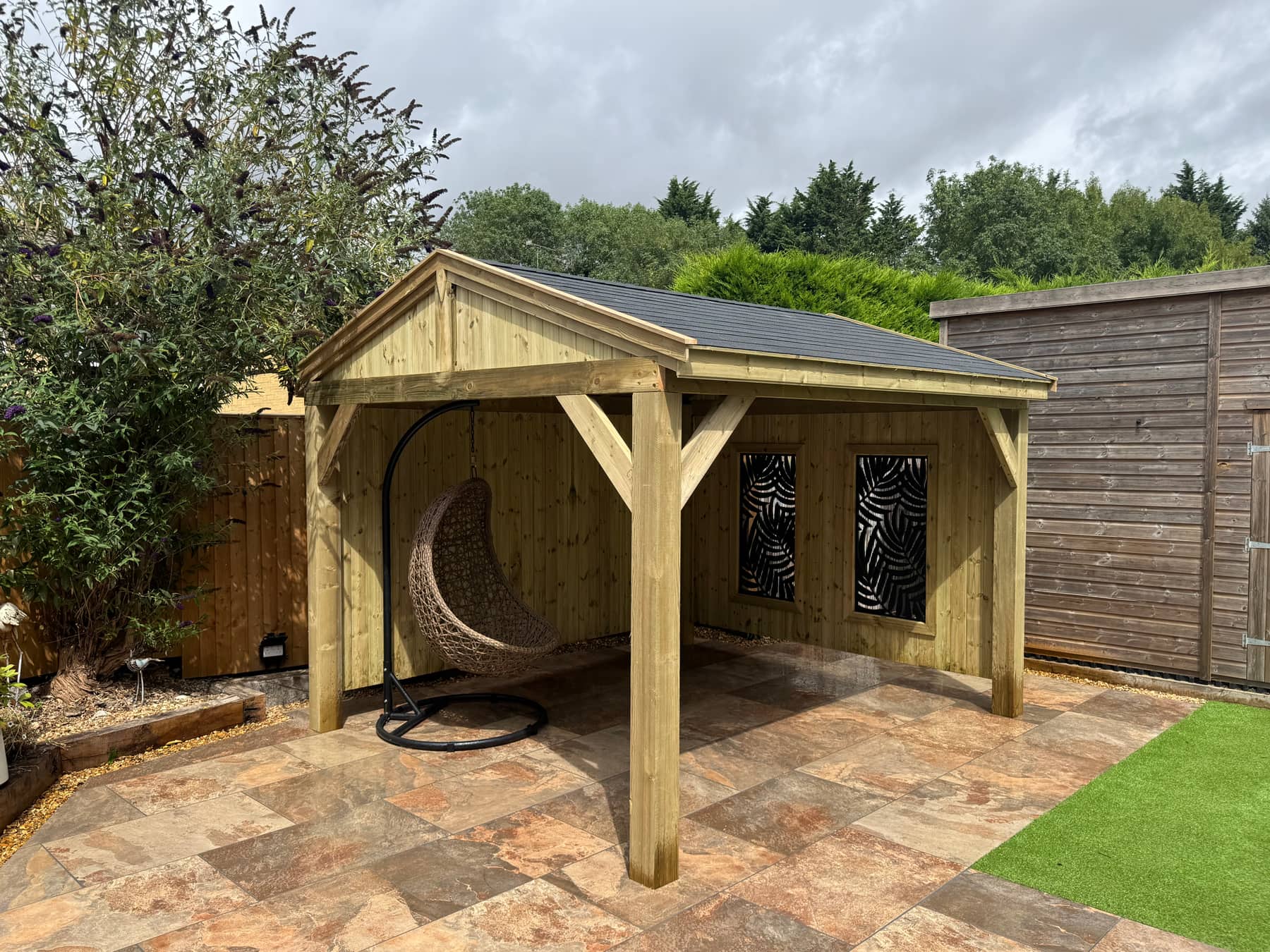 The Kensington, a handcrafted timber gazebo with a gabled roof and decorative privacy panels, on a tiled patio